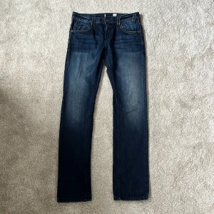 Mörkblå jeans med kontrastsömmar - Snygga mörkblå jeans med raka ben och klassiska kontrastsömmar. Jeansen har fem fickor, bälteshällor och subtila slitningar för en cool look. Perfekta för dig som gillar en tidlös stil och vill ha ett par jeans som funkar till allt. Modellen är slim fit och passar dig perfekt som är 164-170cm lång. 