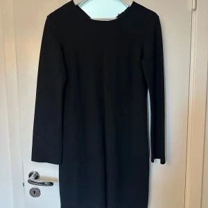 Svart långärmad klänning från Dagmar - En stilren svart klänning från Dagmar i storlek 34. Klänningen har lång ärm och rak passform med enkel, minimalistisk design. Perfekt för dig som gillar klassiska och tidlösa plagg. Tillverkad i ett mjukt material som känns skönt mot huden.