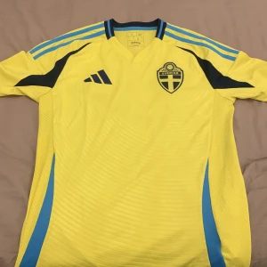 Svensk landslagströja Adidas gul Size s - Gul fotbollströja från Adidas i slim fit, officiell Sverige landslagströja med blå detaljer och svarta inslag. Broderat landslagsemblem på bröstet och klassiska Adidas-ränder på axlarna. Tillverkad i lätt och ventilerande material. TAR BARA KONTANT, SKRIV VART KAN MÖTAS