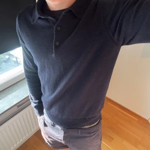 Mörkblå kashmir pikétröja Lodenfrey - Exklusiv mörkblå pikétröja från Lodenfrey i 100% kashmir. Tröjan har klassisk krage, tre knappar framtill och långärmad design. Mjuk och lyxig känsla, perfekt för dig som gillar stilrena och tidlösa plagg.