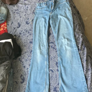 Ljusblå flared jeans från H&M - Säljer ett par ljusblå jeans från H&M med flared ben och låg midja. Jeansen har justerbar midja och klassisk femficksdesign. Perfekta för dig som gillar retrovibbar och vill ha en snygg siluett. Materialet är mjukt denim i bomull.