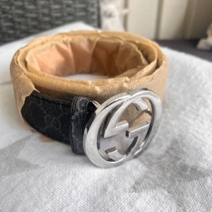 Svart GG bälte - Snyggt svart bälte med klassiskt GG-mönster och ett spänne i silverfärgad metall.  och bältet har en exklusiv vibe som lyfter vilken outfit som helst. Perfekt för dig som gillar designeraccessoarer.
