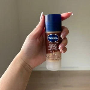 Vaseline Cocoa Shimmer Jelly Stick - Helt ny, oanvänd. Säljs inte i Sverige , köpt i USA. Vaseline Cocoa Shimmer Jelly Stick ger huden en glowig finish med en hint av shimmer. Stiftet är brunt med guldskimmer och har en praktisk twist-up-funktion. Perfekt att ta med i väskan för snabb återfuktning och lyster. Innehåller 40g och doftar kakao. 
