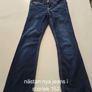 Mörkblå bootcut jeans stl 152 152 - Snygga mörkblå jeans med bootcut-modell och markerade vita sömmar. Klassisk femficksdesign och dekorativa bakfickor med knappar. Perfekta för dig som gillar en lite vidare passform nertill. Materialet är jeans i bomull.