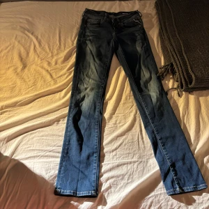 Blå jeans från Replay, modell Vicky - Säljer ett par snygga blå jeans från Replay, modell Vicky. Jeansen har klassisk femficksdesign, raka ben och ljus brun  kontrastsöm på bakfickorna. Materialet är jeans med en mörkblå tvätt och subtila slitningar. Perfekta för dig som gillar en tidlös och stilren look.