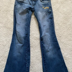 Blåa lågmidjade  jeans med broderi - Snygga blå jeans från Reals med bootcut/ rak passform och broderade detaljer på fickor och fram. De är sydda lite mer lågmidjade men inget som syns. Lite trasiga längst ner men man kan alltid sy upp eller klippa av om man vill. Bra längd på mig som är 175. Pris går att diskuteras.