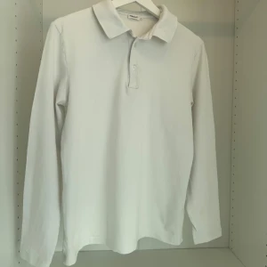 Vit långärmad pikétröja Filippa K - Klassisk vit långärmad pikétröja från Filippa K. Tröjan har krage, knäppning med två knappar och är gjord i mjuk bomull. Perfekt för en clean och stilren look. Passar dig som gillar enkel och tidlös stil.