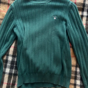 Grön ribbstickad tröja från Gant - Mörkgrön ribbstickad tröja från Gant med broderad logga på bröstet. Tröjan har rund halsringning och långa ärmar. 