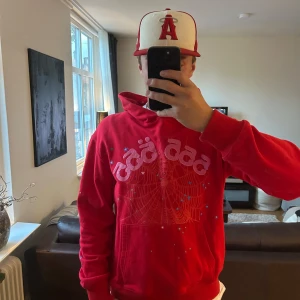Sp5der 555 Hoodie - Röd hoodie från Young thugs märke spider 555 . Tröjan har huva, magficka och långa ärmar. Materialet känns mjukt och skönt, perfekt för chill dagar. Snygga detaljer med små stjärnor på framsidan och ena armen. (Inte äkta därav priset)