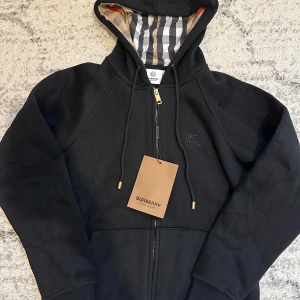 Burberry zip hoodie svart - Helt oanvänd, jätte bra kvalite på den. Passar perfekt för både kalla och varma dagar. Den är storlek S men sitter som XS, hade rekommenderat den för folk med mindre kroppsstorlek.