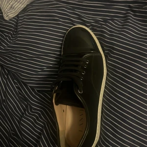 Svarta sneakers från Lanvin - Snygga svarta sneakers från Lanvin med vit sula och klassisk snörning. Skorna har en stilren design i blankt skinn och rund tå. Perfekta för dig som vill ha en clean och lyxig look till vardags. Diskret branding på insidan.