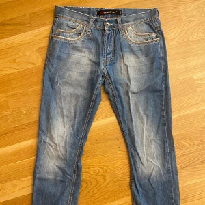 Blå jeans från Cipo & Baxx med detaljer - Snygga blå jeans från Cipo & Baxx med slitningar och kontrastsömmar. Klassisk femficksmodell, coola bakfickor med broderade detaljer och läderpatch i midjan. Jeansen har normal passform och är tillverkade i jeansmaterial.