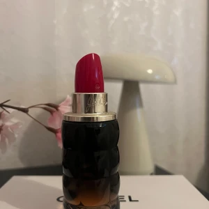  CacharelYes I Am EdP - Cool parfymflaska från Cacharel designad som ett läppstift med svart och brun glasbotten och silverdetaljer. Toppen är formad som ett rött läppstift, vilket gör flaskan till en snygg inredningsdetalj på sminkbordet.