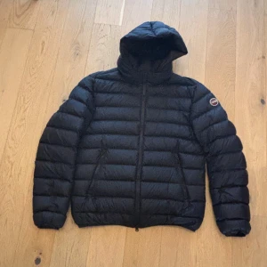 Mörkblå dunjacka med huva från Colmar - Säljer en svart dunjacka från Colmar med huva och horisontella sömmar. Jackan har dragkedja framtill, två sidofickor och en innerficka med dragkedja. Kvitto finns, Knappt använd och köptes inför förra säsongen.