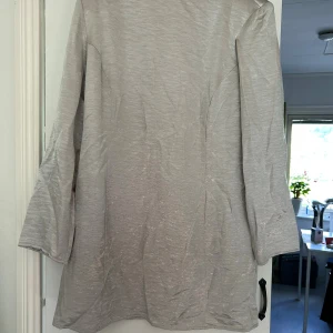 Beige kortklänning med öppen rygg - Säljer en beige kortklänning med långärmade ärmar och en djup, öppen rygg. Klänningen har en enkel, rak passform och är tillverkad i ett lätt, slätt material som ger en stilren look. Perfekt för dig som gillar minimalistisk design och vill sticka ut med en snygg ryggdetalj.