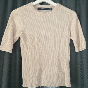 Beige stickad tröja från Vero Moda - Säljer en beige stickad tröja från Vero Moda i storlek XS. Tröjan har ribbad struktur, rund halsringning och halvlånga ärmar. Perfekt för lager-på-lager och enkel att matcha med både jeans och kjol.