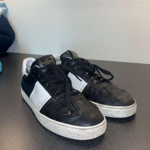 Valentino Garavani svartvita sneakers - Svartvita sneakers från Valentino Garavani i skinn med klassisk låg siluett. Skorna har svarta snören, vit sula med små nitar baktill och logga på plösen. Snygg kontrast mellan svart och vitt, samt cool detalj med mönstrad yttersula.