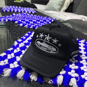 Corteiz Keps - Snygg svart truckerkeps med silvriga broderade stjärnor och motiv framtill. Kepsen har mesh på sidorna och bak för extra ventilation. Justerbar passform och cool streetkänsla, perfekt för dig som vill sticka ut.