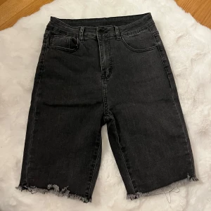Mörk gråa  jeansshorts från SHEIN storlek M - Mörk gråa  jeansshorts från SHEIN med hög midja och råa, fransiga benslut. Klassisk femficksmodell med dragkedja och knapp framtill. Perfekta för en chill och avslappnad look under sommaren.