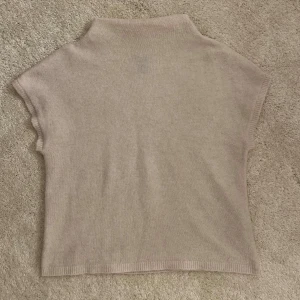 Beige stickad polotröja från Lindex - En stilren beige stickad polotröja från Lindex i storlek S. Tröjan har korta ärmar och en hög krage, perfekt för lager-på-lager. Mjuk och skön känsla, passar till både jeans och kjol för en chill look.