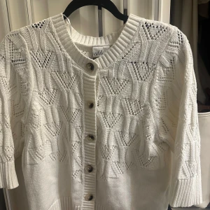 Vit stickad kofta från Isolde - Superfin vit stickad kofta från Isolde med snyggt hålmönster och ribbade muddar. Koftan har knappar framtill och trekvartsärmar, perfekt för lager på lager. Nypris 500kr. 