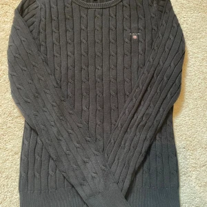 Svart kabelstickad tröja från Gant - Kabelstickad svart tröja från Gant i stretchig bomull. Detta är ett damplagg och är ganska liten i storleken. Egentligen är den k storlek S men jag väljer att sätta den som xs eftersom att det är såpass liten