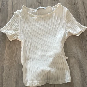 Vit ribbad topp med knyt från FB Sister - Säljer en vit ribbad topp från FB Sister i storlek XS. Toppen har korta ärmar, rund halsringning och snygg knytning i ryggen. Tillverkad i mjuk bomull och passar perfekt till jeans eller kjol för en fräsch look.