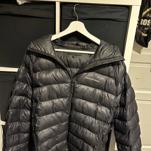 Svart dunjacka Peak Performance M men passar S - Säljer en svart dunjacka från Peak Performance i storlek M. Jackan har en snygg quiltad design, huva och dragkedja framtill. Broderad logga på bröstet och ärmen. Perfekt för kalla dagar och riktigt skön att bära.