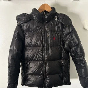 Polo Ralph Lauren puffer glossy - Svart glossy puffer jacka från Polo Ralph Lauren i storlek XS. Väldigt bra skick, endast använd under januari-februari. NYPRIS: 5600kr, MITT PRIS: 2099kr. Priset är ej hugget i sten. Hör gärna av dig vid frågor!😊