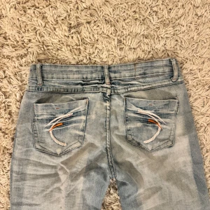 Ljusblå jeans med broderade bakfickor - Säljer ett par ljusblå jeans från Marble Jeans med coola slitningar och broderade detaljer på bakfickorna i vitt och orange. De är bootcut och lågmidjade💞hör av er om ni har några frågor!!