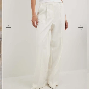 Vita vida kostymbyxor med pressveck - Snygga vita kostymbyxor med vida ben och pressveck framtill. Byxorna har hög midja, hällor för bälte och diskreta fickor. Perfekta för en clean och stilren look. Helt oanvända med etiketten kvar på, säljer då de är fel stl och jag inte hann göra retur i tid. inköpt för 600kr, mitt pris 400kr