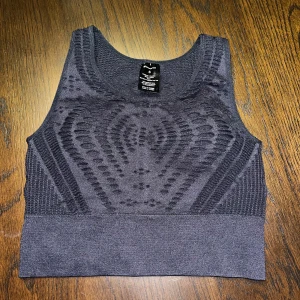 Svart crop tank från Energetics - Säljer en svart crop tank från Energetics med snyggt geometriskt mönster i ryggen och bred resår nedtill. Toppen är ärmlös och har en sportig vibe, perfekt för träning eller chill. Materialet är stretchigt och följsamt för maximal komfort.
