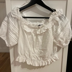 Vit blus med volang - Supersöt vit blus från H&M med volangdetaljer vid halsringning och nederkant. Blusen har puffiga korta ärmar med spetsinslag och resår, samt en offshoulder-modell, croppad modell💕