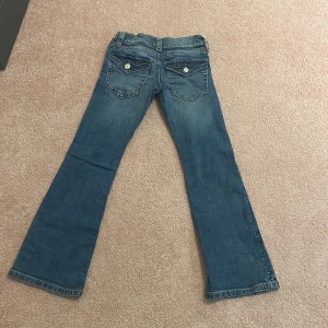 Blå bootcut jeans från Gina Tricot - Snygga blå jeans från Gina Tricot i storlek 140. Modellen har bootcut-ben, klassiska fickor med lock och knapp både fram och bak samt coola kontrastsömmar. Har använt dem max två gånger. Jeansen är tillverkade i denim och har låg midja för en trendig look.