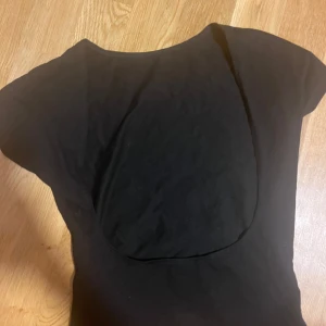 Svart öppen rygg topp - En enkel svart topp med öppen rygg och  korta ärmar och rund halsringning. Toppen är figurnära och tillverkad i mjukt bomullsmaterial, perfekt att matcha med jeans eller kjol för en clean look.