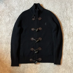 Pringle of scotland cardigan svart  - Säljer denna svarta stickade cardiganen gjort på 100% lamm ull från märket Pringle of Scotland. Cardiganen har unika funktionella knappar gjort på fårskinn, ribbade muddar/krage etc och har 2st fickor längre ner. Håller värmen mycket bra och perfekt att ha för lager-på-lager nu i höst/vinter. Stilren och unik som enkelt går att matcha med det mesta. En storlek L men har man en tröja under så sitter den perfekt som en M. Nypris: 5k+. Varmt välkommen att kontakta vid frågor/funderingar. mvh DC 🔹