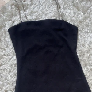 Svart kort klänning med strassband - Supersnygg svart kort klänning från H&M med tunna axelband i strass. Klänningen har en enkel, tight passform och ärmlös design. Perfekt för dig som vill sticka ut med lite extra bling på axlarna. Materialet är mjukt och följsamt.