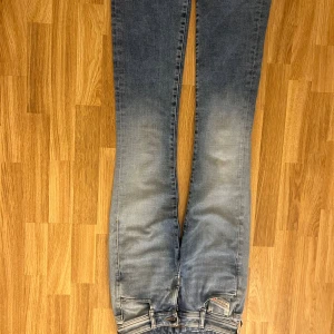 Blå raka jeans från Diesel - Snygga blå jeans från Diesel med raka ben och klassisk femficksdesign. Jeansen har ljus tvätt med slitningar och detaljer som synliga sömmar och dragkedja. Perfekta för dig som gillar en avslappnad men stilren look.
