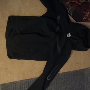 Svart Nike tech hoodie med dragkedja - Har knappt använt sen jag köpte pågrund av att den är för liten.                                  Svart hoodie från Nike i storlek S med hel dragkedja framtill och huva. Tröjan har diskreta reflexdetaljer på bröstet och ärmen samt en praktisk ficka med dragkedja på ärmen. Perfekt för träning eller chill. Klassisk Nike-logga på bröstet.