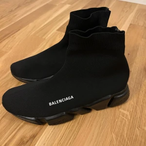 Balenciaga Speed Trainer sneakers svarta - Svarta Balenciaga Speed Trainer sneakers med stickad ovandel i syntetmaterial och chunky svart sula. Strumpliknande passform med ribbad kant och Balenciaga-logga på sidan och hälen. Snygg futuristisk vibe och superbekväma att bära.