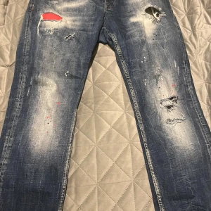 Philipp Plein blå  jeans - Säljer ett par blå jeans från Philipp Plein med coola slitningar, hål och färgstänk i rött. Jeansen har en rak passform och klassisk femficksdesign. Märkespatch bak på linningen. Perfekta för dig som gillar streetstyle och unika detaljer.