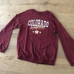 Vinröd tröja - Säljer en vinröd tröja  med tryck 'Colorado Longmont' i vitt och guld på bröstet. Tröjan har långa ärmar, rund halsringning och är gjord i mjuk bomull. Perfekt för en chill och avslappnad stil. Använt men bra skick 👍 