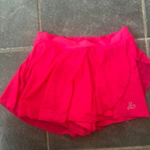 Konståknings kjol  - Snygga chockrosa omlottshorts från Intermezzo i storlek S. Lätta och luftiga med volangig känsla och glittrande stenar i form av ett hjärta på ena benet. Perfekta för dans eller träning när du vill sticka ut.