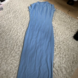 Ljusblå långklänning med kort ärm - Enkel och stilren ljusblå långklänning med korta ärmar och rund halsringning. Klänningen har en rak passform och är tillverkad i ett mjukt, tunt material som känns skönt mot huden. Perfekt för varma dagar eller när du vill ha en clean look.