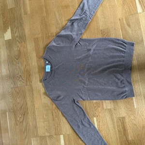 Beige stickad tröja från Bläck - En stilren beige stickad tröja från Bläck i storlek S. Tröjan har rund halsringning, ribbade muddar och lång ärm. Perfekt för lager-på-lager och enkel att matcha med jeans eller chinos.