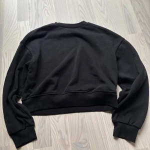 Svart sweatshirt från H&M Divided - En svart, basic sweatshirt från H&M Divided med rund halsringning och ribbade muddar vid ärmslut och nederkant. Tröjan har en loose passform och är tillverkad i mjuk bomullsmix. 