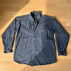 Blå skjorta från Polo Ralph Lauren - Klassisk blå skjorta från Polo Ralph Lauren i 100% bomull. Skjortan har lång ärm, knappar hela vägen och ikonisk röd broderad logga på bröstet. Perfekt oversized fit för en avslappnad stil. Bra vintage skick, utan hål eller märken