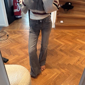 Grå bootcut jeans med låg midja - Snygga grå jeans med bootcut och låg midja. Jeansen har klassisk femficksdesign, dragkedja och knapp framtill. Materialet är mjukt denim som sitter skönt och ger en avslappnad vibe. Perfekta för dig som gillar en retroinspirerad look.