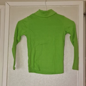 Grön polotröja från Lupilu - Grön polotröja från Lupilu i mjuk bomull. Tröjan har lång ärm och klassisk polokrage, perfekt för lager-på-lager under kyligare dagar. Enkel och stilren design som passar till det mesta.