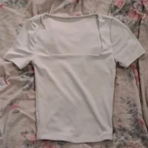 Vit topp med fyrkantig halsringning - Vit topp med korta ärmar och snygg fyrkantig halsringning. Enkel och stilren design som passar till många olika outfits. Toppens material känns mjukt och stretchigt, vilket gör den bekväm att bära hela dagen.